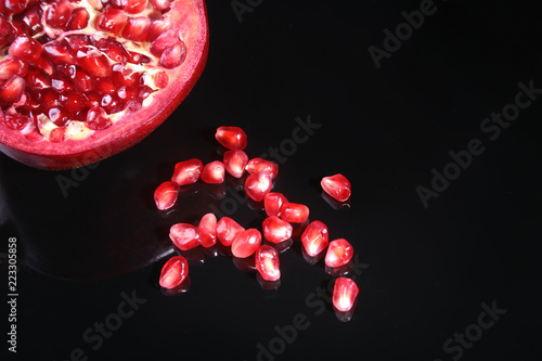Pomegranate seeds and Beautiful ripe pomegranate on black mirror background with place for copy space. photo