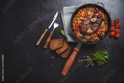 Ready-cooked meat on the bone Osso Buco in tomato sauce over black background of cast iron photo
