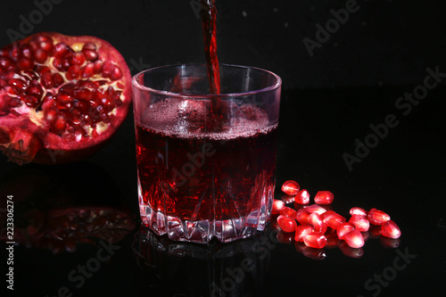 Glass with pomegranate juice Pomegranate seeds and Beautiful ripe pomegranate on black mirror background with place for copy space.
