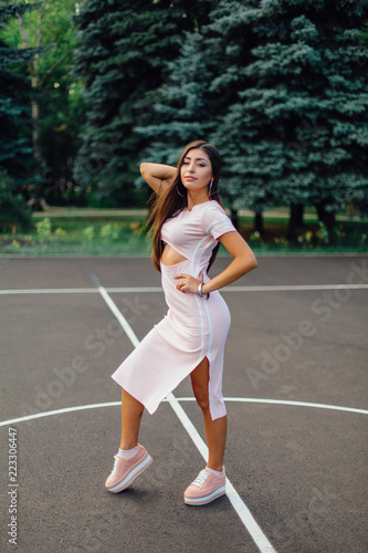 Charming brunette female dressed in a pink dress posing on the basketball court. © Smile