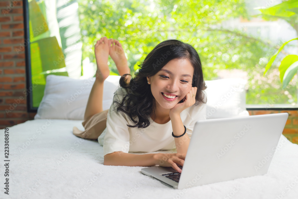 Naklejka premium Pretty asian woman using laptop computer in bed in room and smiling