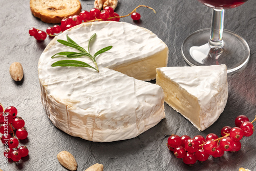 A photo of Camembert cheese with a glass of red wine, fruits and nuts, shot on a black background with copy space