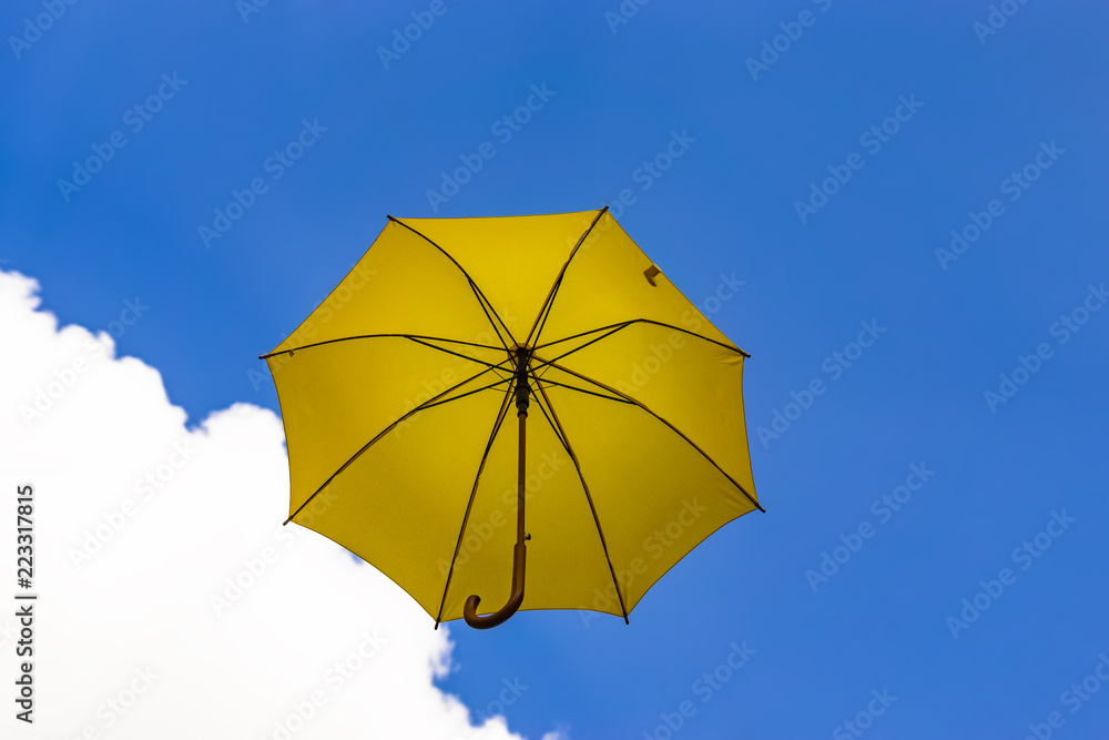 Flying yellow umbrella on a blue sky with white cloud 