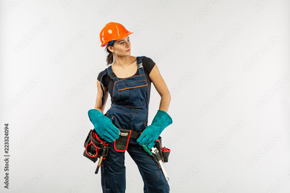 Construction work and home improvement jobs concept with a caucasian brunette mature woman wearing helmet or hard hat, tool belt and other safety equipment on white Construction work and home improvement jobs concept with a caucasian brunette mature woman wearing helmet or hard hat, tool belt and other safety equipment on white