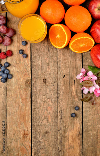 Fototapeta Naklejka Na Ścianę i Meble -  Orange juice, fresh oranges, apples, grapes, raspberries, blueberries and spring flowers on a wooden table - view from above - vertical photo