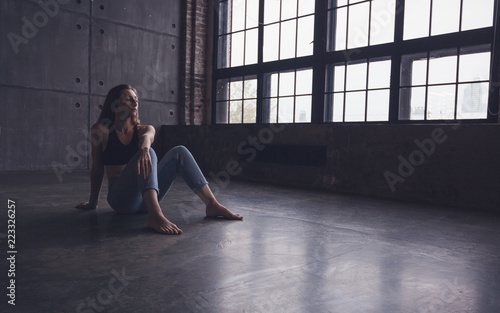 young beautiful woman dancer contemporary in tops and jeans sits on the floor in dance studio