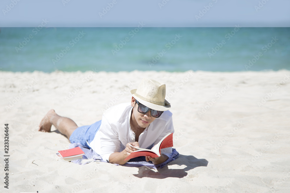 Young Asian man happy smiling and read books on the beach. Pretty hansom asian in casual looking away and smile , laughing.Remote tropical beaches and countries. travel concept man relaxing on beach.