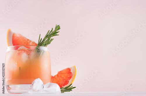 Cold grapefruit cocktail decorated twig rosemary and slice citrus closeup on pink background.