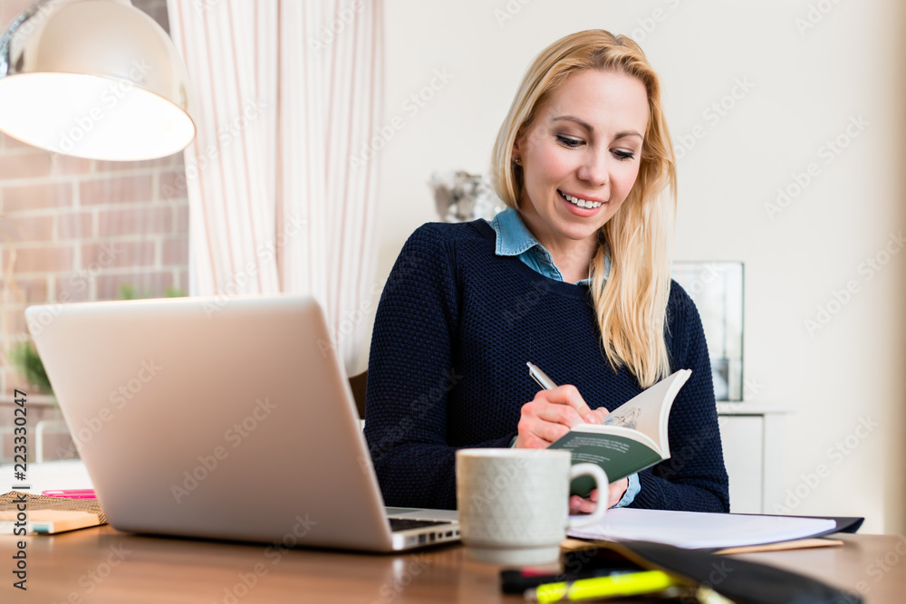 Portrait of a smiling woman at her desk writing on book Portrait of a smiling woman at her desk writing on book