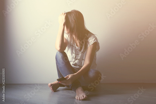 Teenager girl with depression sitting alone on the floor in the dark room. Toned