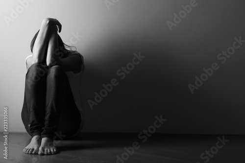 Teenager girl with depression sitting alone on the floor in the dark room.  Black and white photo photo