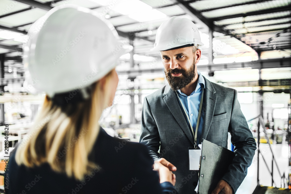 A portrait of an industrial man and woman engineer in a factory, shaking hands. A portrait of an industrial man and woman engineer in a factory, shaking hands.