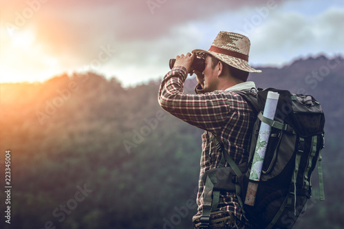 hiker with backpack standing looking through binoculars on the mountain photo