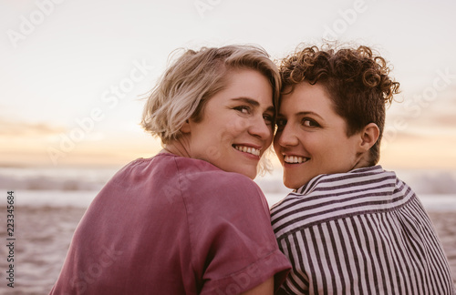 Smiling young lesbian couple watching a romantic beach sunset