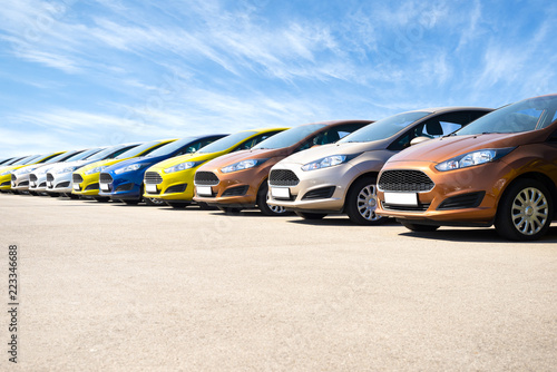 Vibrant new cars for sale stock lot row against blue sky at the sunrise