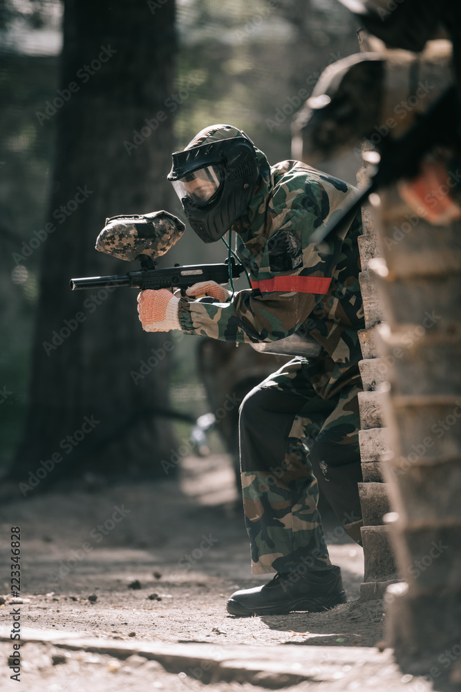 Fototapeta premium selective focus of male paintball player in goggle mask and camouflage aiming by paintball gun outdoors
