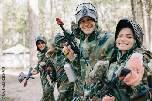 smiling young male paintballer embracing female teammate in camouflage with paintball gun outdoors photo