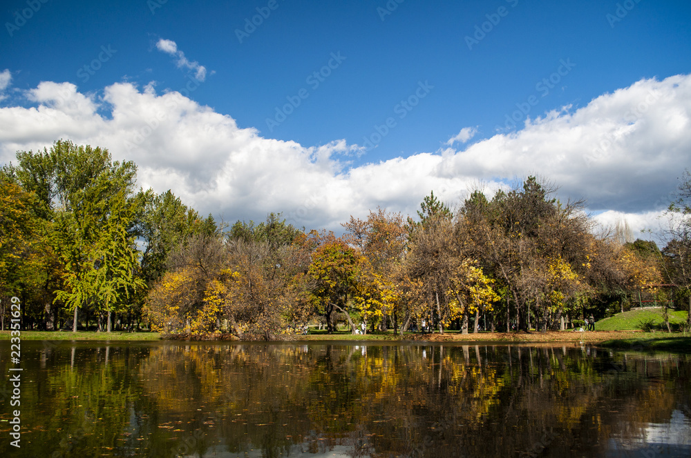 Beautiful autumn park with colorful trees and leaves and reflection in artificial ponds.