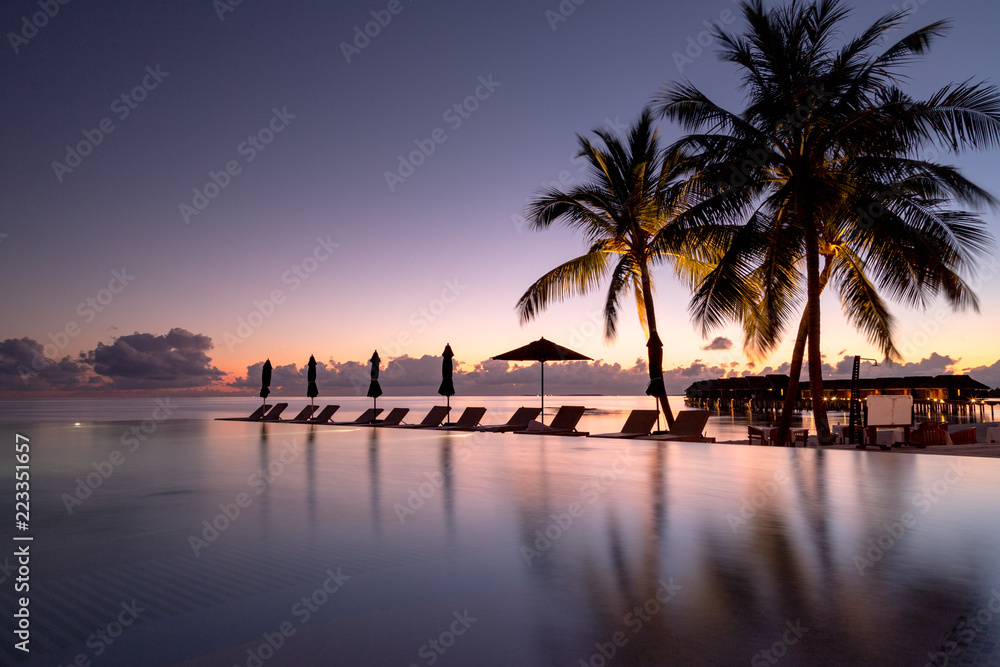 Obraz premium Beautiful poolside and sunset sky. Luxurious tropical beach landscape, deck chairs and loungers and water reflection.
