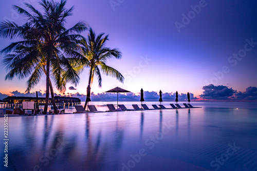 Fototapeta Naklejka Na Ścianę i Meble -  Beautiful poolside and sunset sky. Luxurious tropical beach landscape, deck chairs and loungers and water reflection.
