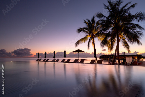 Beautiful poolside and sunset sky. Luxurious tropical beach landscape  deck chairs and loungers and water reflection.