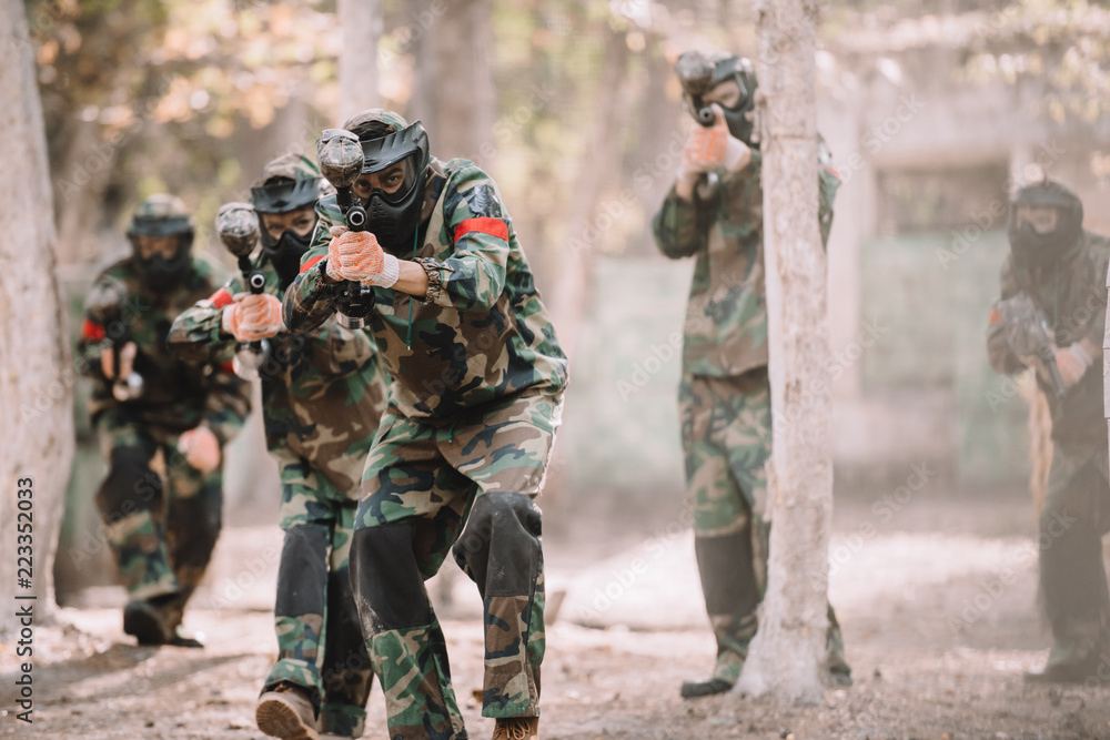 Fototapeta premium paintball team in uniform and protective masks aiming by paintball guns outdoors