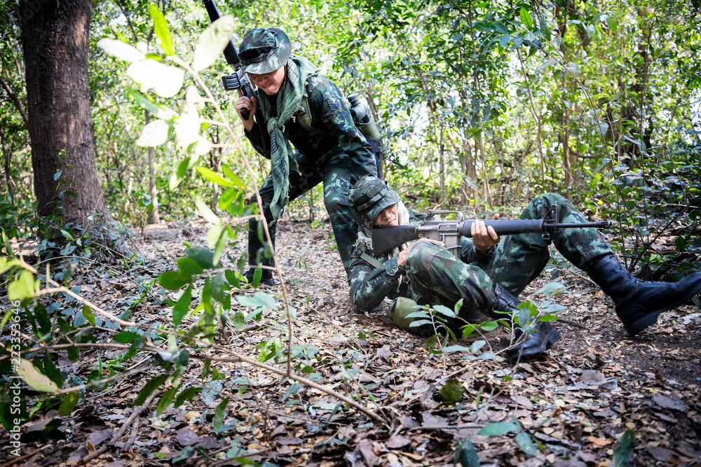 Asian army soldier with weapon during rescue operation evacuate injured fellow at across the deep forest.
