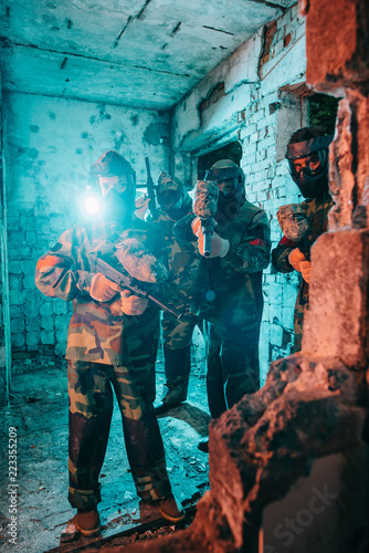 paintball team in uniform and protective masks with paintball guns in abandoned building