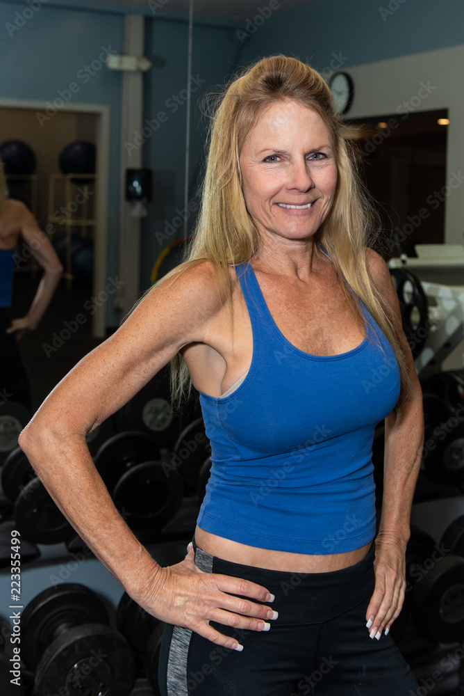 Smiling middle age female content with life while posing in health club weight room. Smiling middle age female content with life while posing in health club weight room.