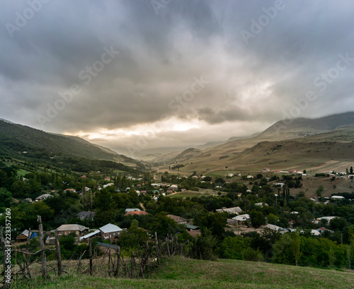 Beautiful mountain village on a background. autumn landscape. Village on the hillside. Forest on the mountain light fall on clearing on mountains at sunset with rainbow



