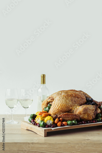 close up view of festive thanksgiving dinner table set with glasses of wine, roasted turkey and vegetables on wooden tabletop on grey backdrop photo