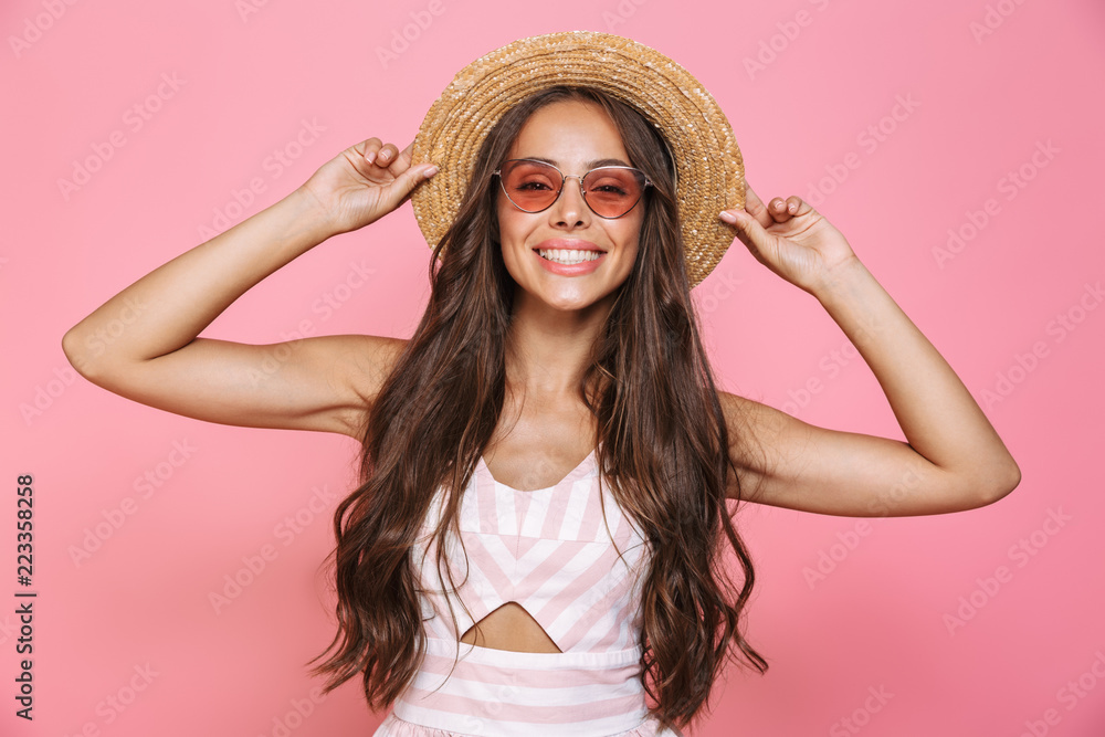 Photo of charming woman 20s wearing sunglasses and straw hat smiling at camera, isolated over pink background Photo of charming woman 20s wearing sunglasses and straw hat smiling at camera, isolated over pink background