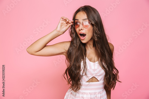 Photo of stylish woman 20s wearing sunglasses looking aside with surprise, isolated over pink background