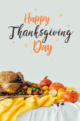 close up view of roasted turkey, pumpkins and happy thanksgiving day lettering on grey background