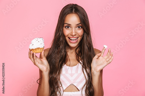 Schilderij op canvas Photo of happy woman 20s wearing dress having fun while eating cupcake, isolated