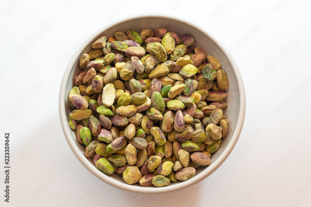 White ceramic bowl of pistachio nuts, centered, isolated on white, horizontal aspect White ceramic bowl of pistachio nuts, centered, isolated on white, horizontal aspect