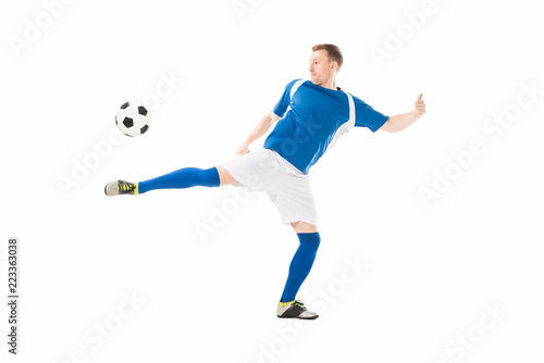 full length view of athletic young soccer player kicking ball isolated on white