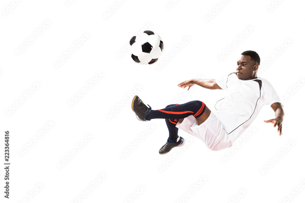 athletic young african american soccer player kicking ball in jump isolated on white