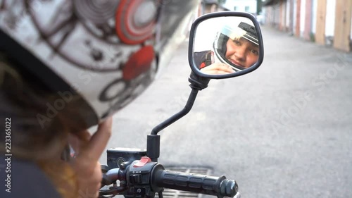woman rider fixing motorcycle helmet rear view, reflectiong in a motorbike mirror photo