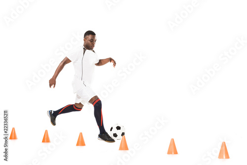 young african american sportsman running and training with soccer ball and marker cones isolated on white photo