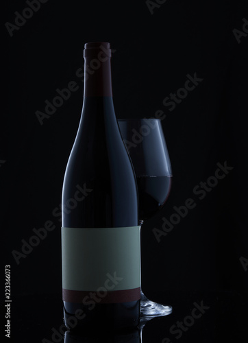 A bottle of wine and a glass with wine on a black background
