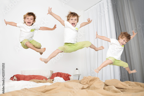 Cheerful little boy  jumping on bed at home. lot of children.
