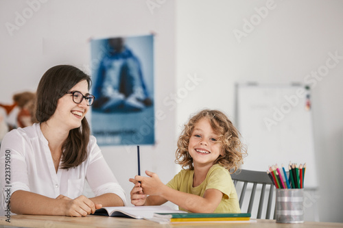 Smiling teacher and happy kid doing homework after classes