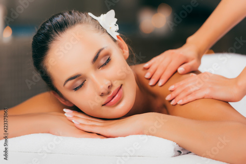 beautiful young woman with flower in hair having massage at spa salon