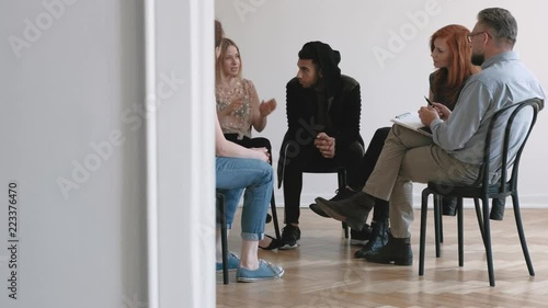 Teenagers and psychotherapist listening to young woman while sitting in the circle during therapy