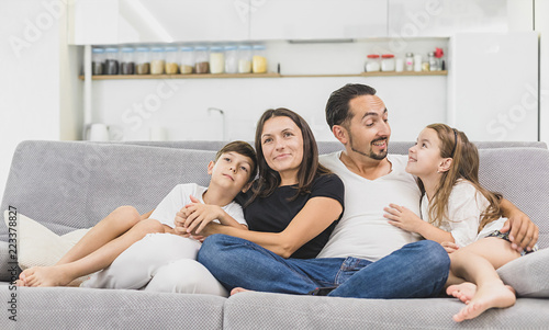 Family sitting on sofa smiling at camera on modern apartment background