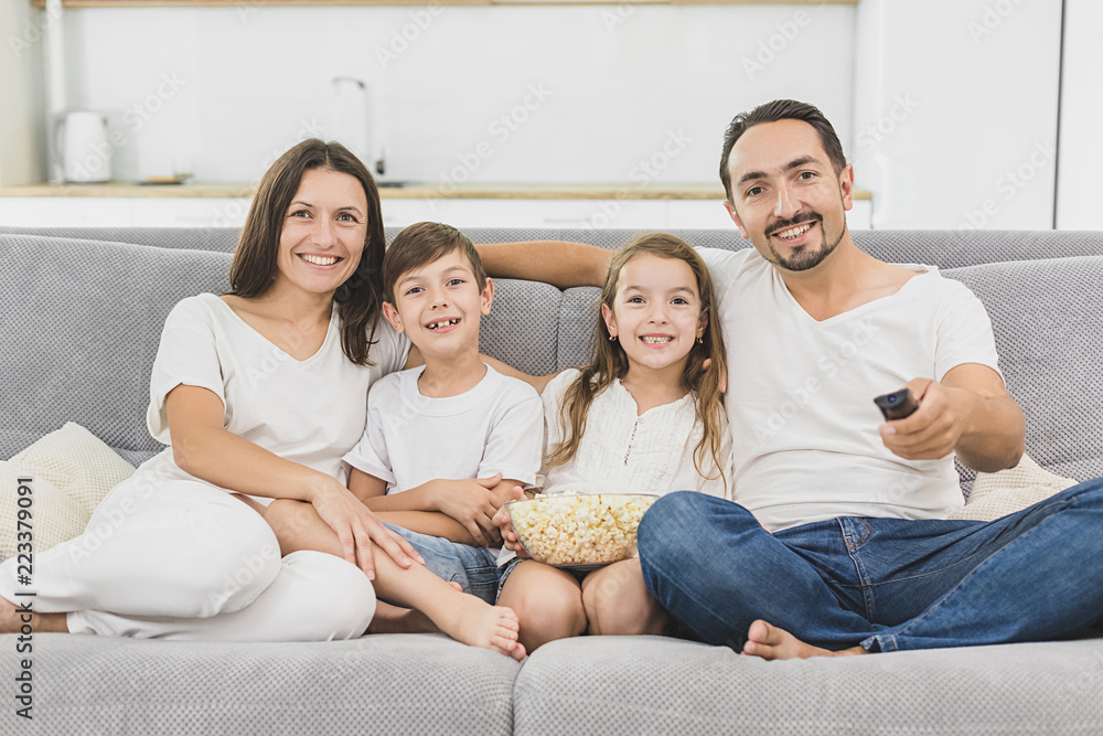 Leisure together. Happy family of four is enjoying at home. Small cute kids, parents are on the sofa, hugging, watching tv Leisure together. Happy family of four is enjoying at home. Small cute kids, parents are on the sofa, hugging, watching tv