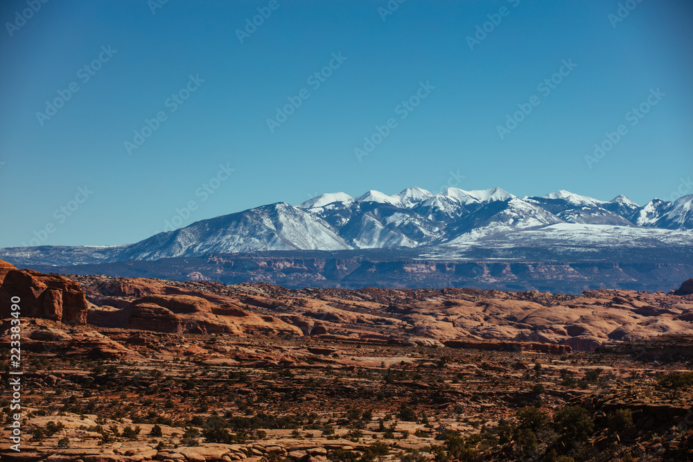 Snow Capped Peaks Over The Red Rock Desert Landscape Of Utah In The Iconic American Southwest