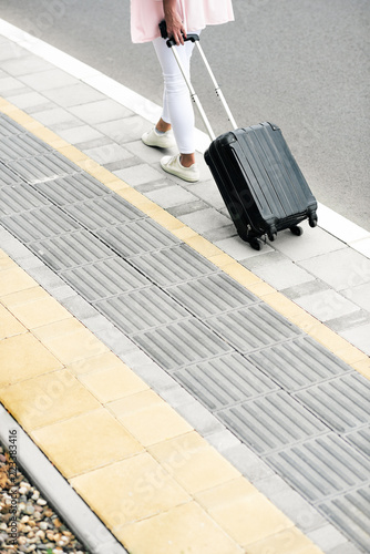 Woman carrying luggage while walking to the station. Back turned.