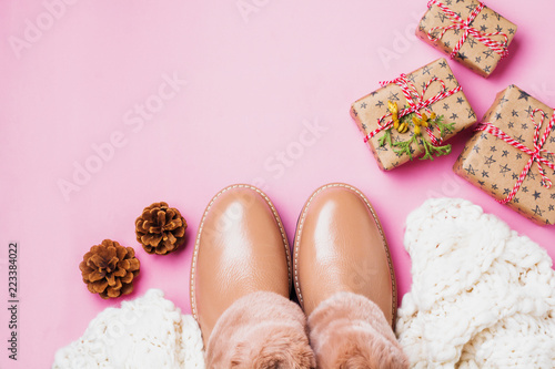 Leather women's warm shoes with fur, white scarf and gifts boxes on light pink background. Сoncept of the New Year season. Top view. Cope space.